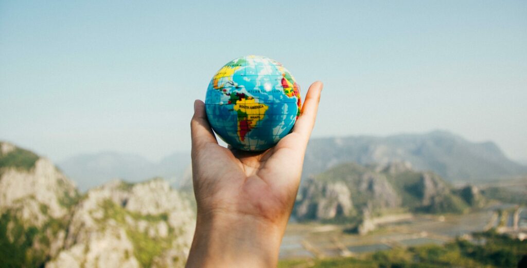 Hand holding a globe against a mountain background symbolizing travel and exploration.