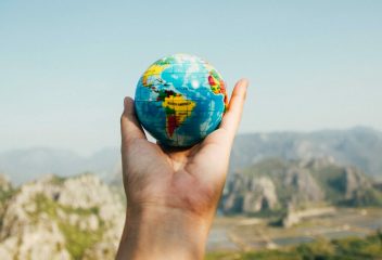 Hand holding a globe against a mountain background symbolizing travel and exploration.